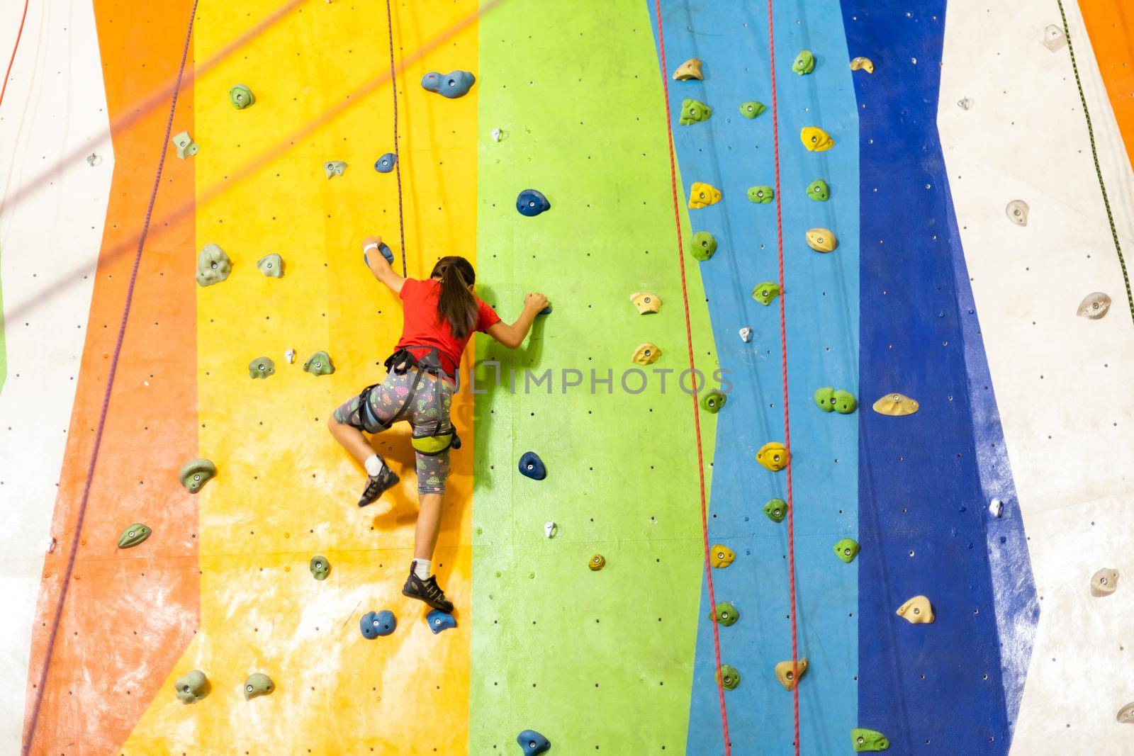Sporty little girl climbing artificial boulder on practical wall in gym