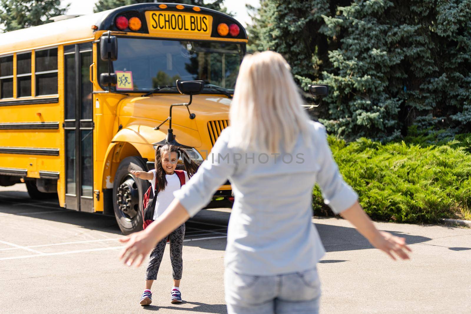 Kids student running into mother's hands to hug her after back to school near the school bus