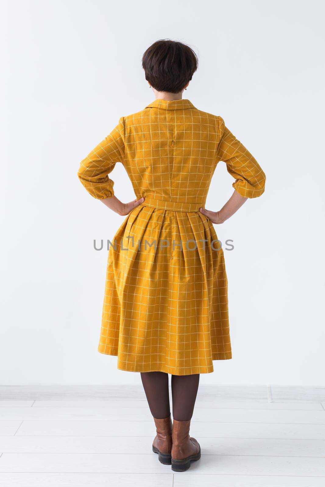 clothing, designer, people concept - back view of attractive woman in a yellow dress posing on white room. by Satura86