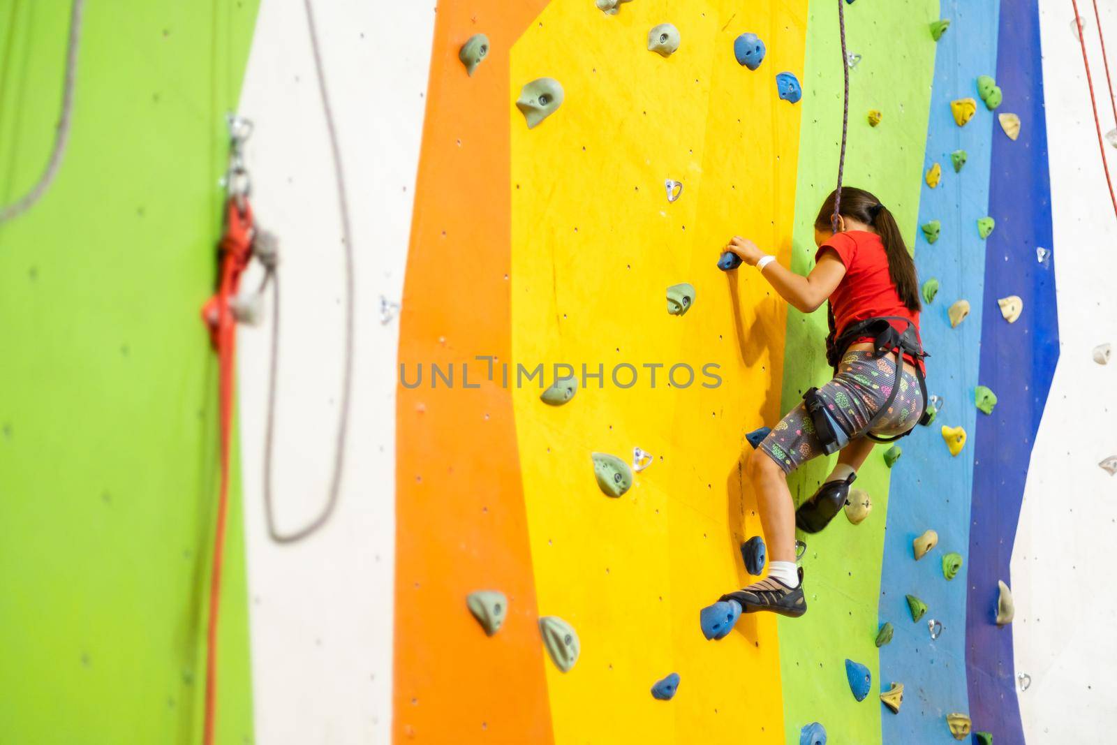 Sporty little girl climbing artificial boulder on practical wall in gym