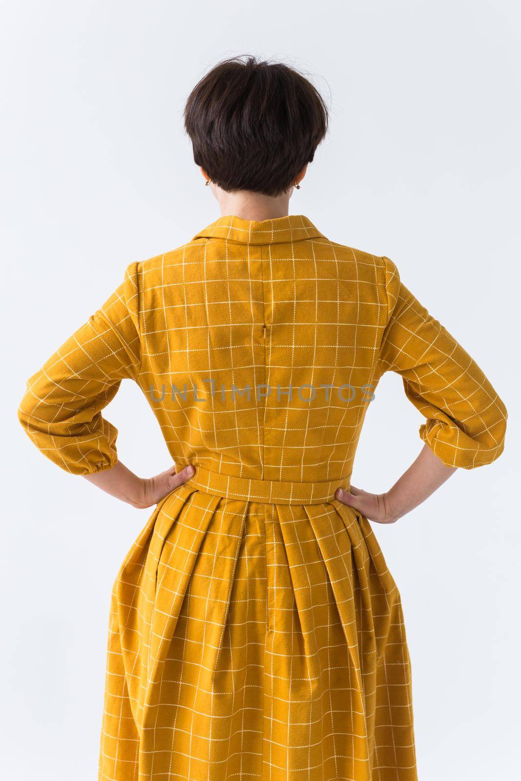 clothing, designer, people concept - back view of attractive woman in a yellow dress posing on white room