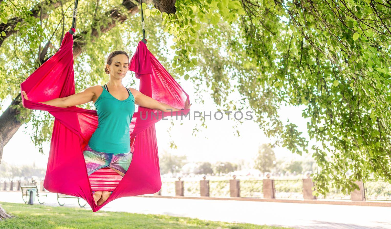 Sport girl doing fly yoga in hammock at nature keeping body in the air. Athlete woman during aero stretching gymnastics outdoors in summer