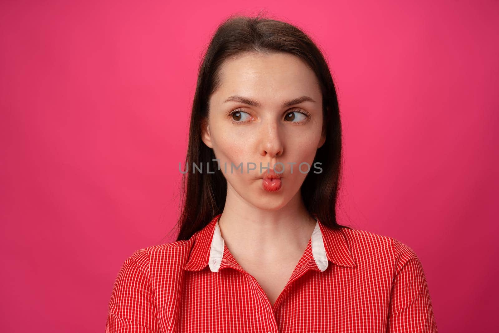 Portrait of pretty young woman sucked in her cheeks against pink background, close up