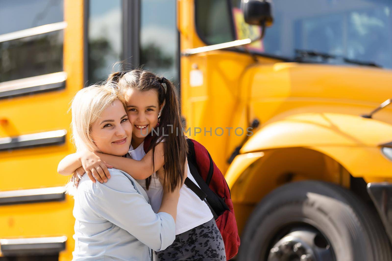 Mother brings her daughter to school near the school bus. back to school