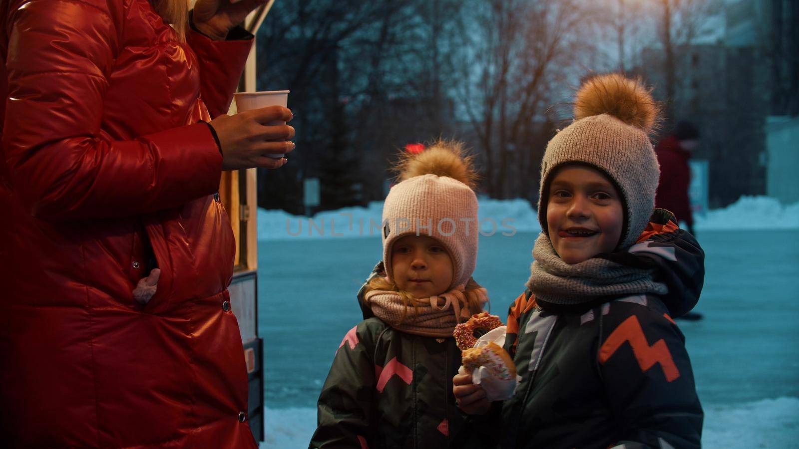 A young woman with her happy children drinking hot drinks and eating donuts. Mid shot