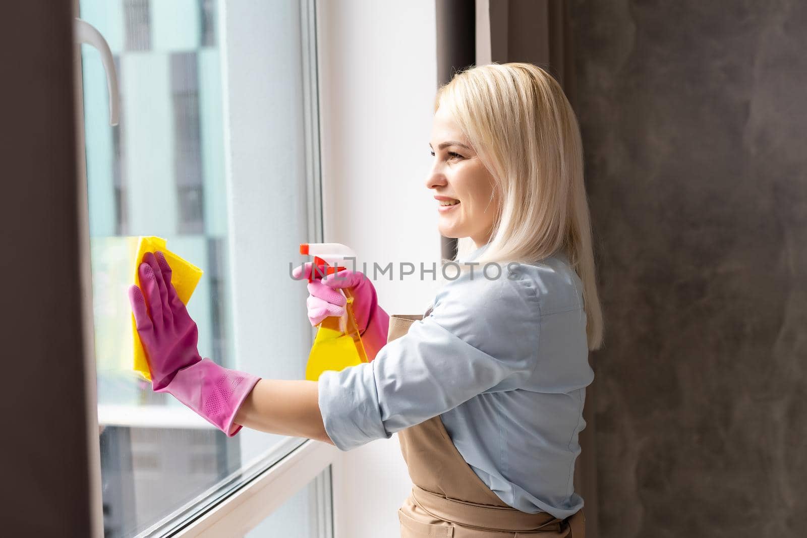 Smiling black woman cleaning windows with glass cleaner
