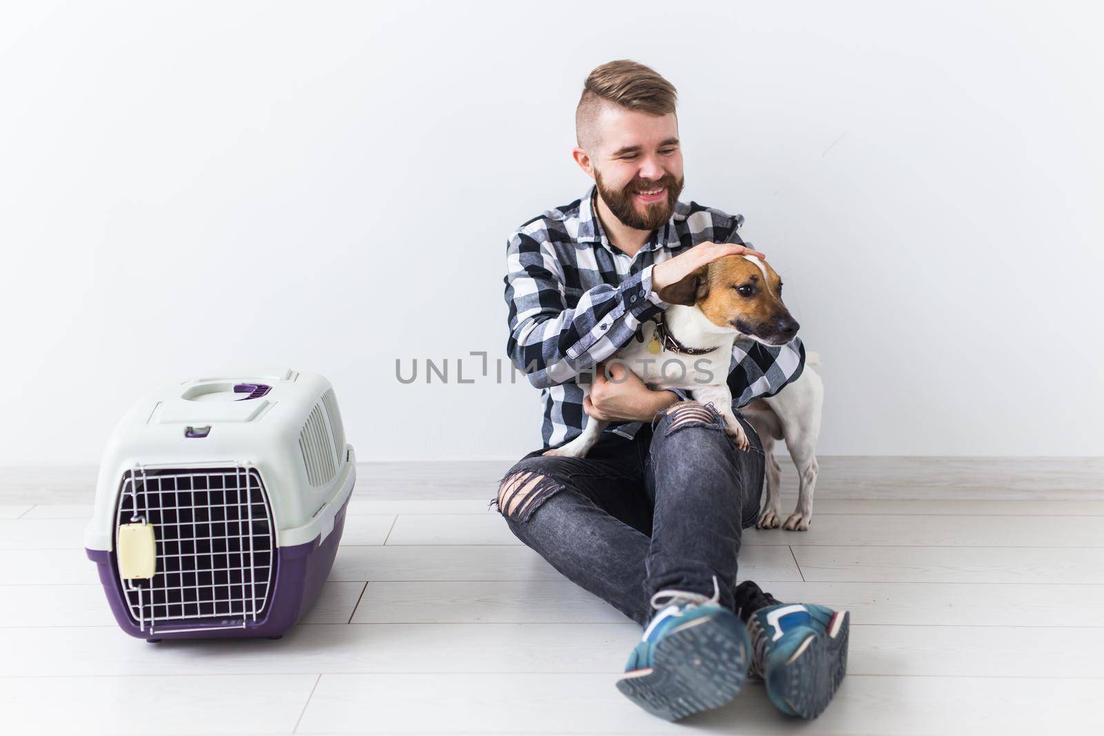 Dog carrying bags and pets owner concept - Attractive cheerful male in plaid shirt holds favourite pet. Happy bearded man with his jack russell terrier.