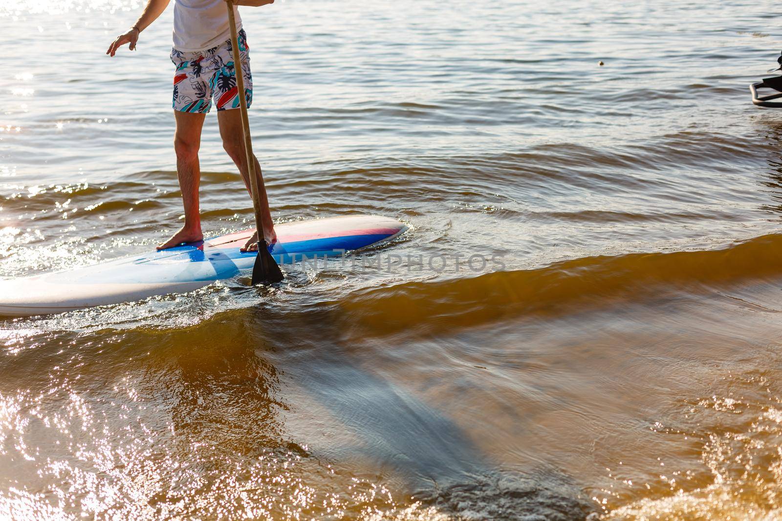 Silhouette of stand up paddle boarder paddling at sunset