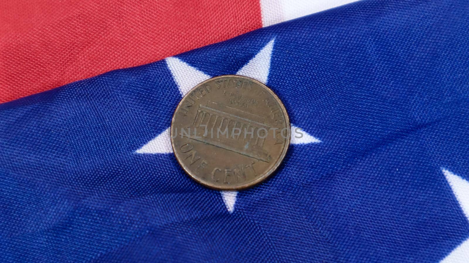 A 1 cent American dollar coin lies on the American flag. The currency is one cent over the flag of the United States