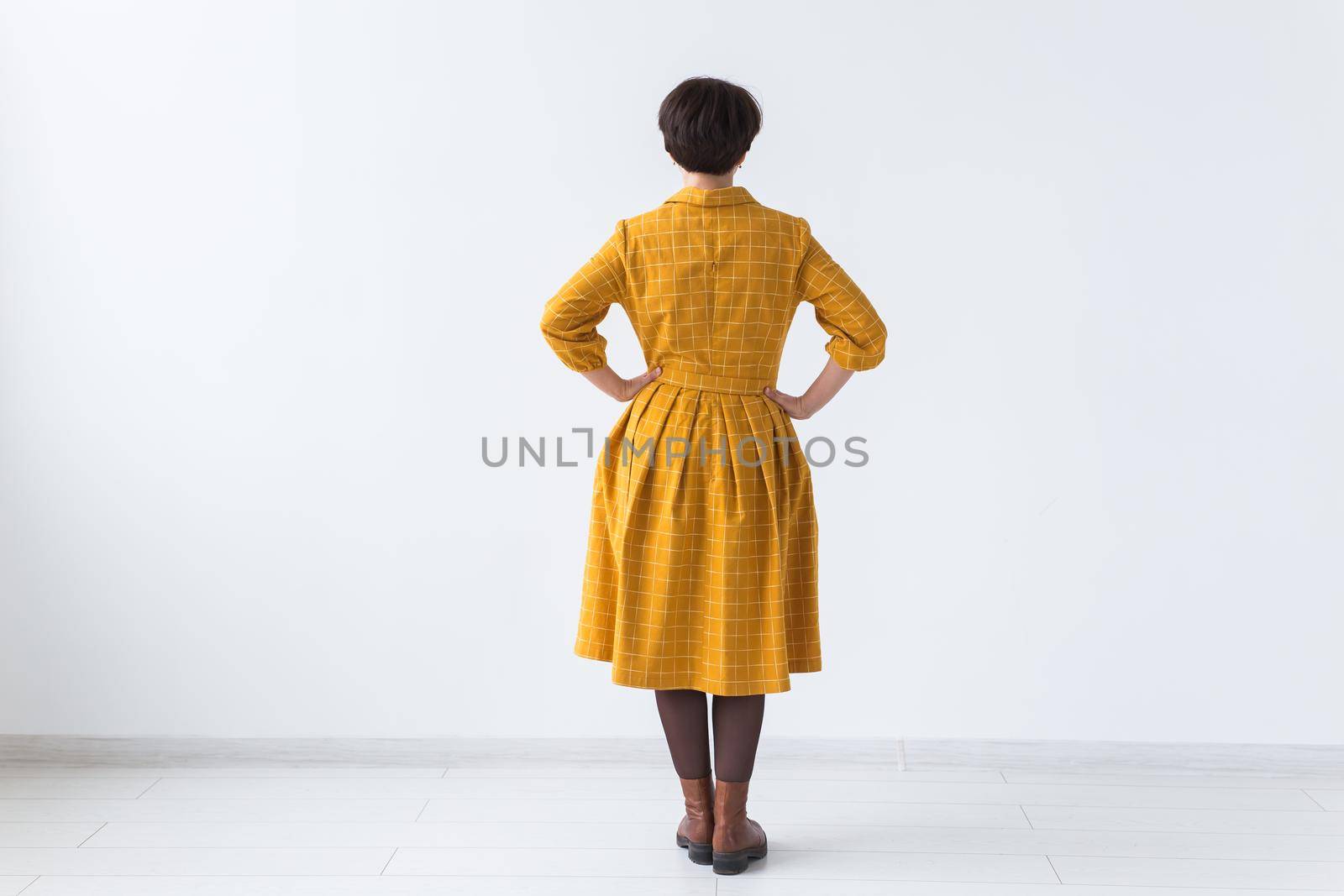 clothing, designer, people concept - back view of attractive woman in a yellow dress posing on white room