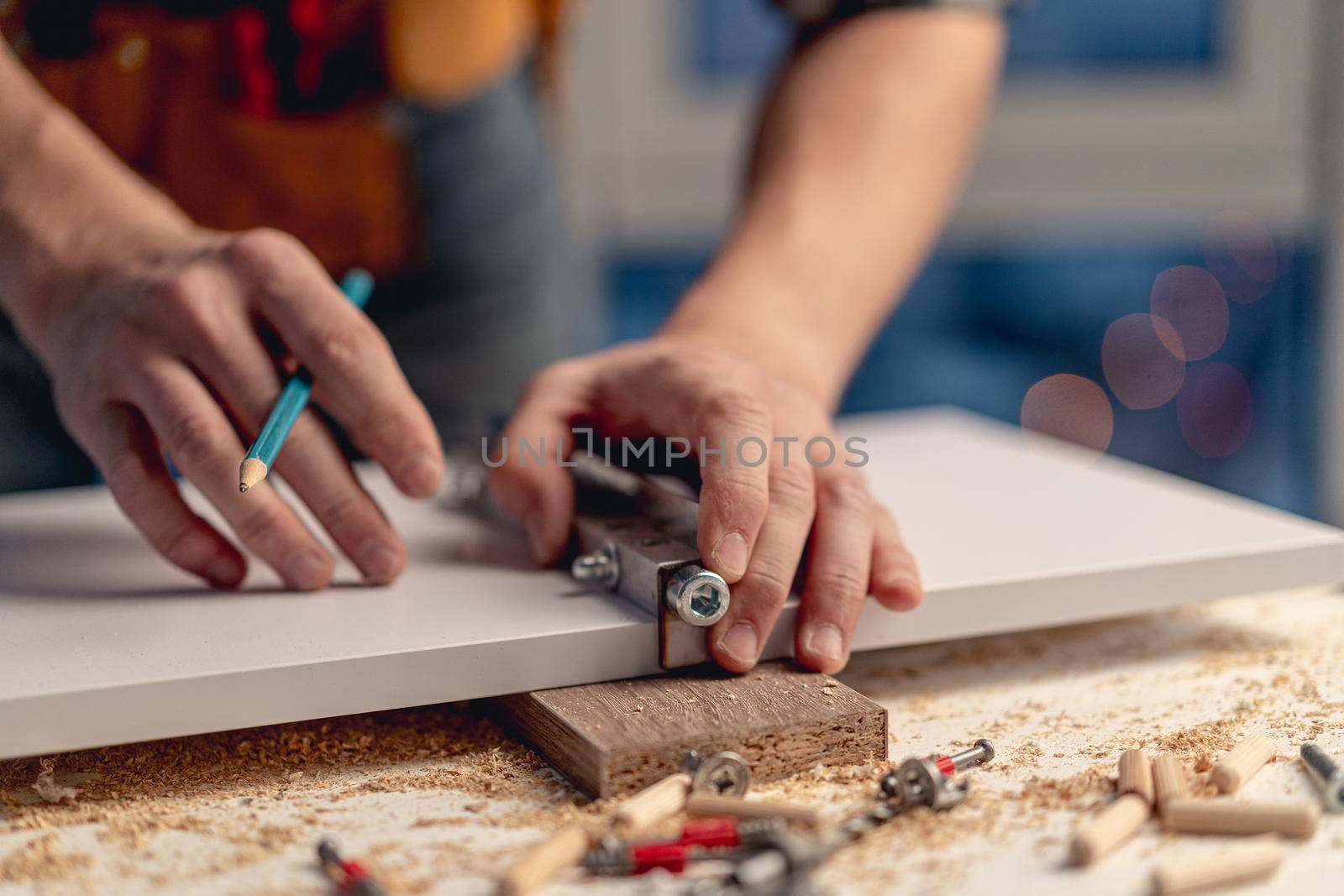 Man working with pencil marking holes during process of wooden furniture manufacturing in workshop