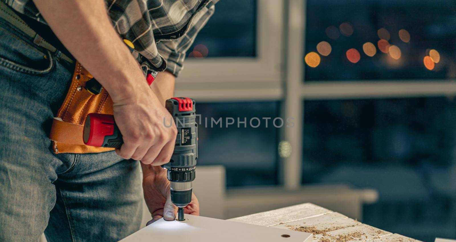 Man working making holes in board with drill during process of furniture manufacturing