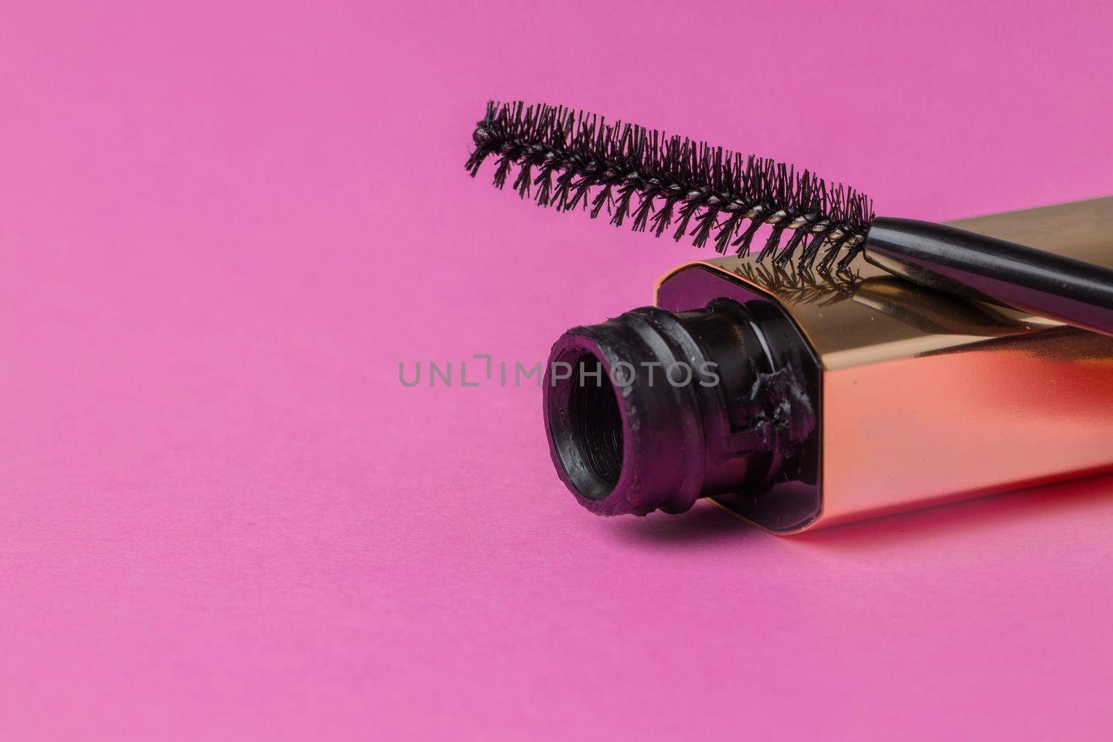 Open gold tube of mascara close up on pink background