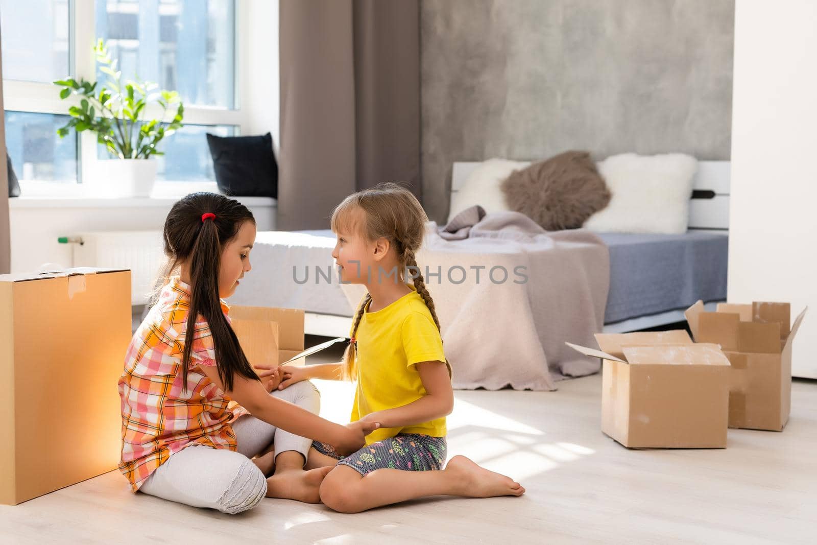 Happy family in living room. Preschool daughters sitting and help unpacking cardboard boxes belongings. Buy real estate, relocation at new modern house