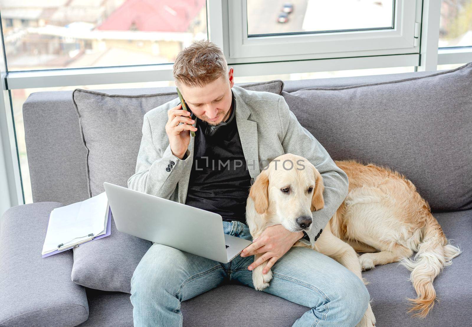 Handsome man cuddling lovely dog while working on sofa in bright room