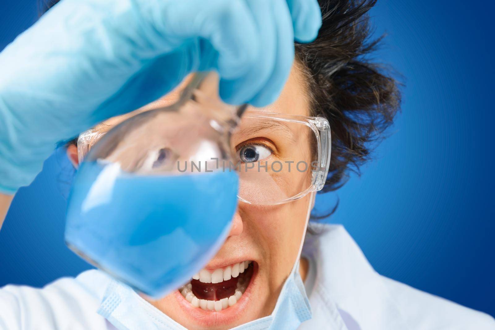 Crazy happy man scientist examines flask with blue liquid