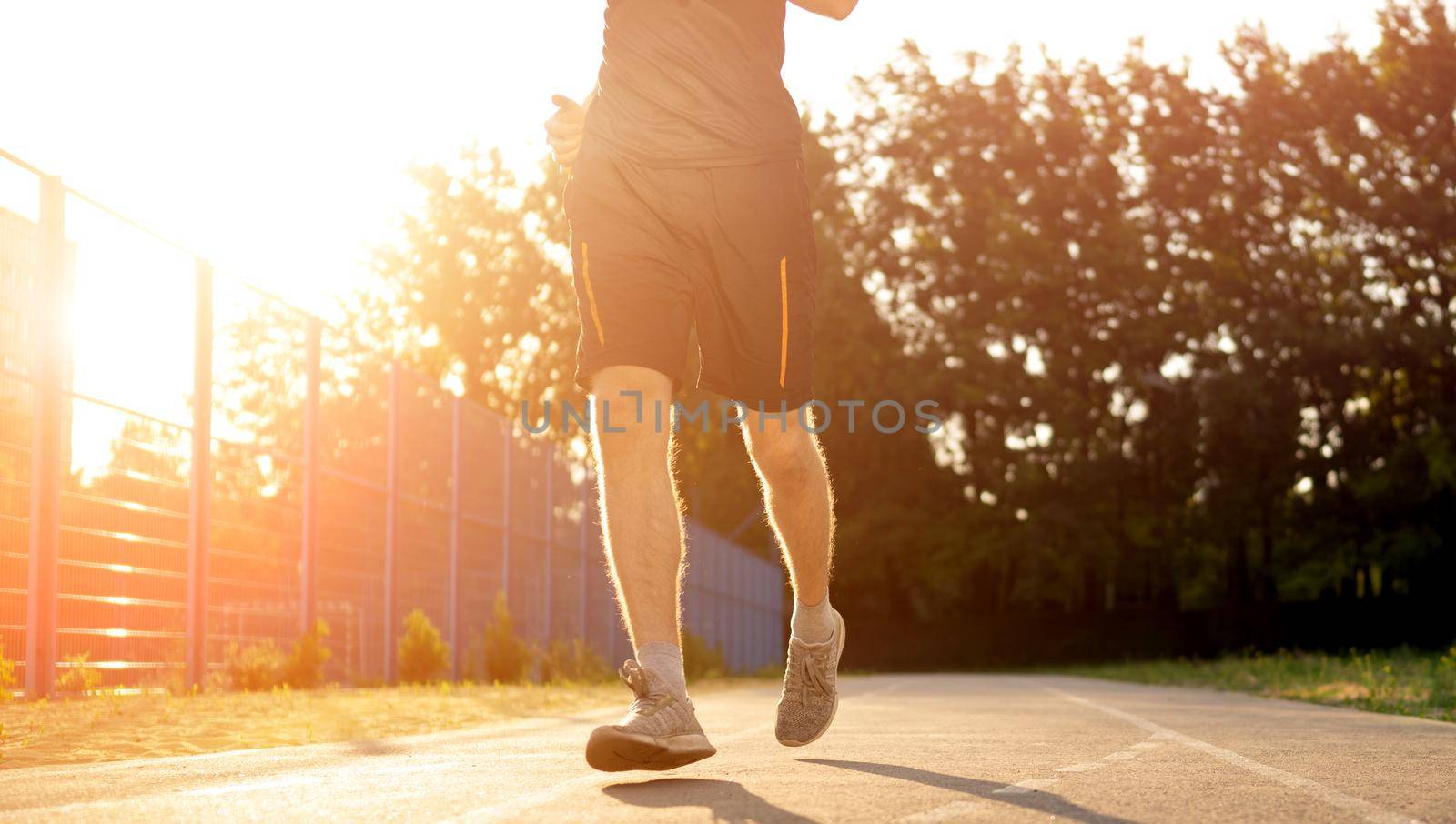 Man guy running with sunlight at the stadium outdoors. Male person during workout. Sportsman exercising