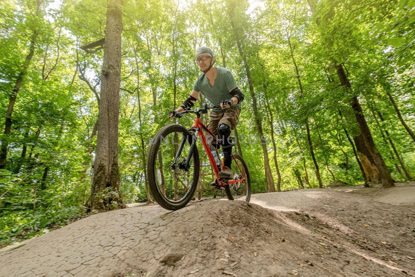 Man riding bicycle on forest road in shadows of high trees