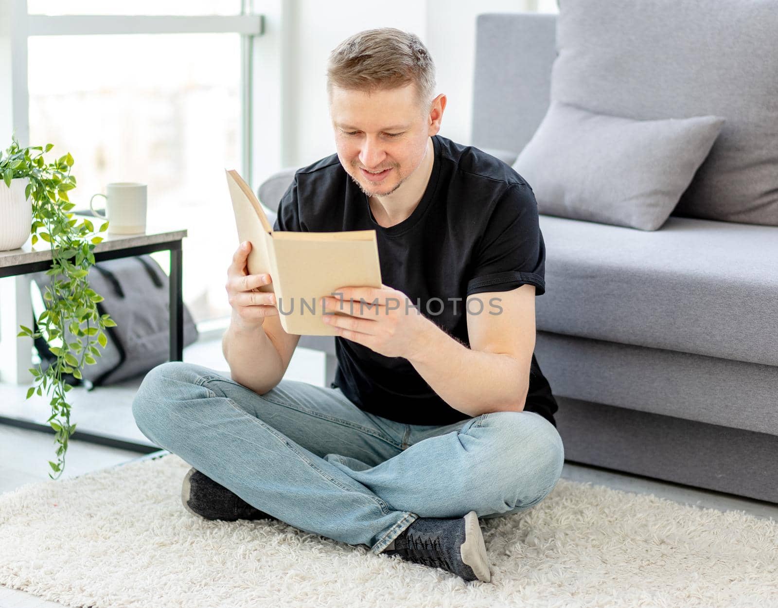 Attractive man reading paper book sitting on floor at home