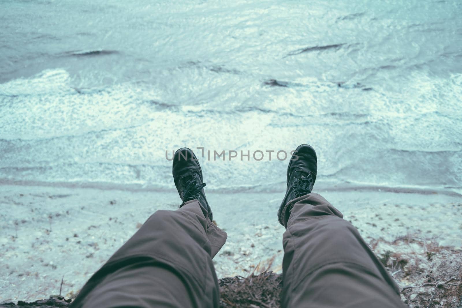 Man sitting on coast above the sea, view of legs. Point of view shot