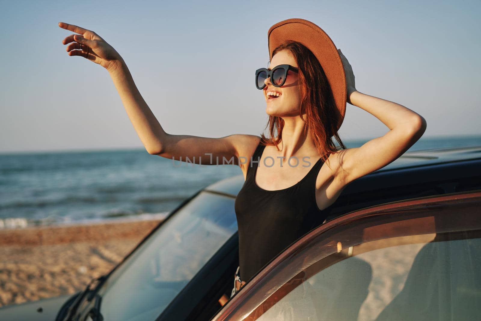 cheerful woman in sunglasses and a hat on the ocean near the car. High quality photo