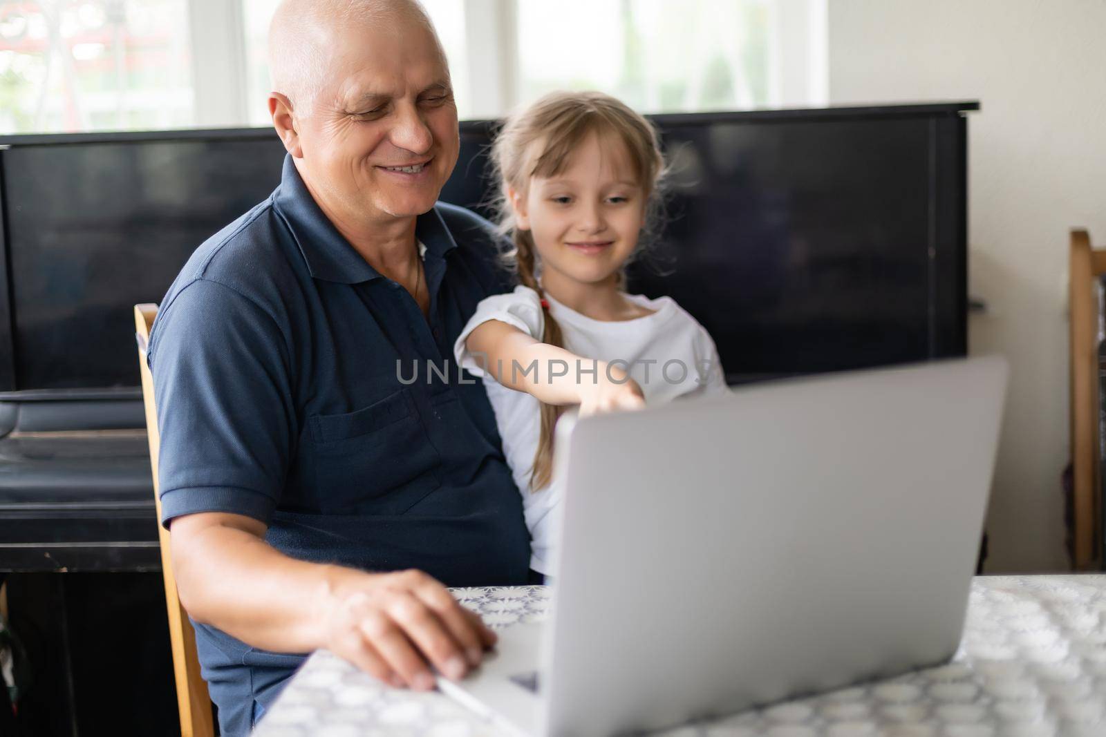 Senior grandfather with small granddaughter indoors sitting at table.