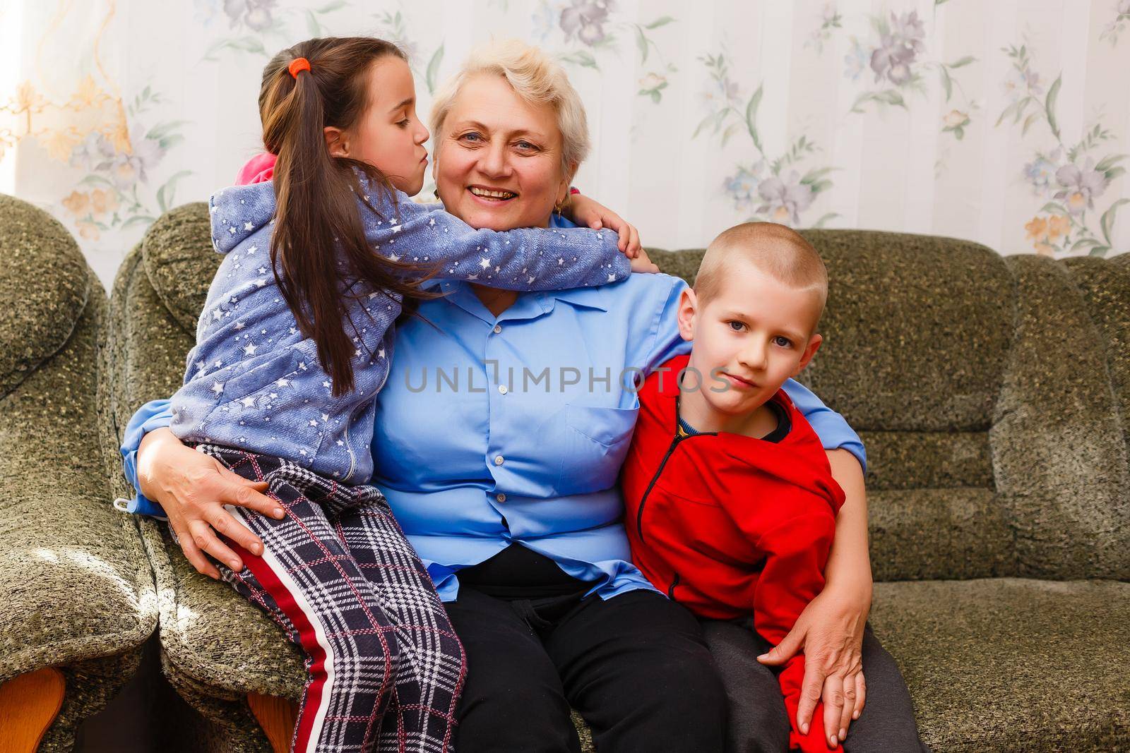 Grandmother and grandchildren sitting together on sofa in living room by Andelov13