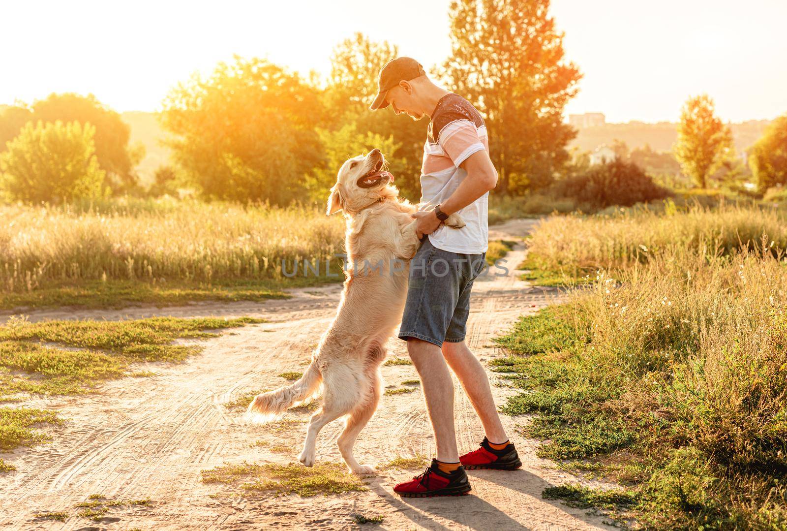 Golden retriever dog standing on back paws next to man outdoors at sunset