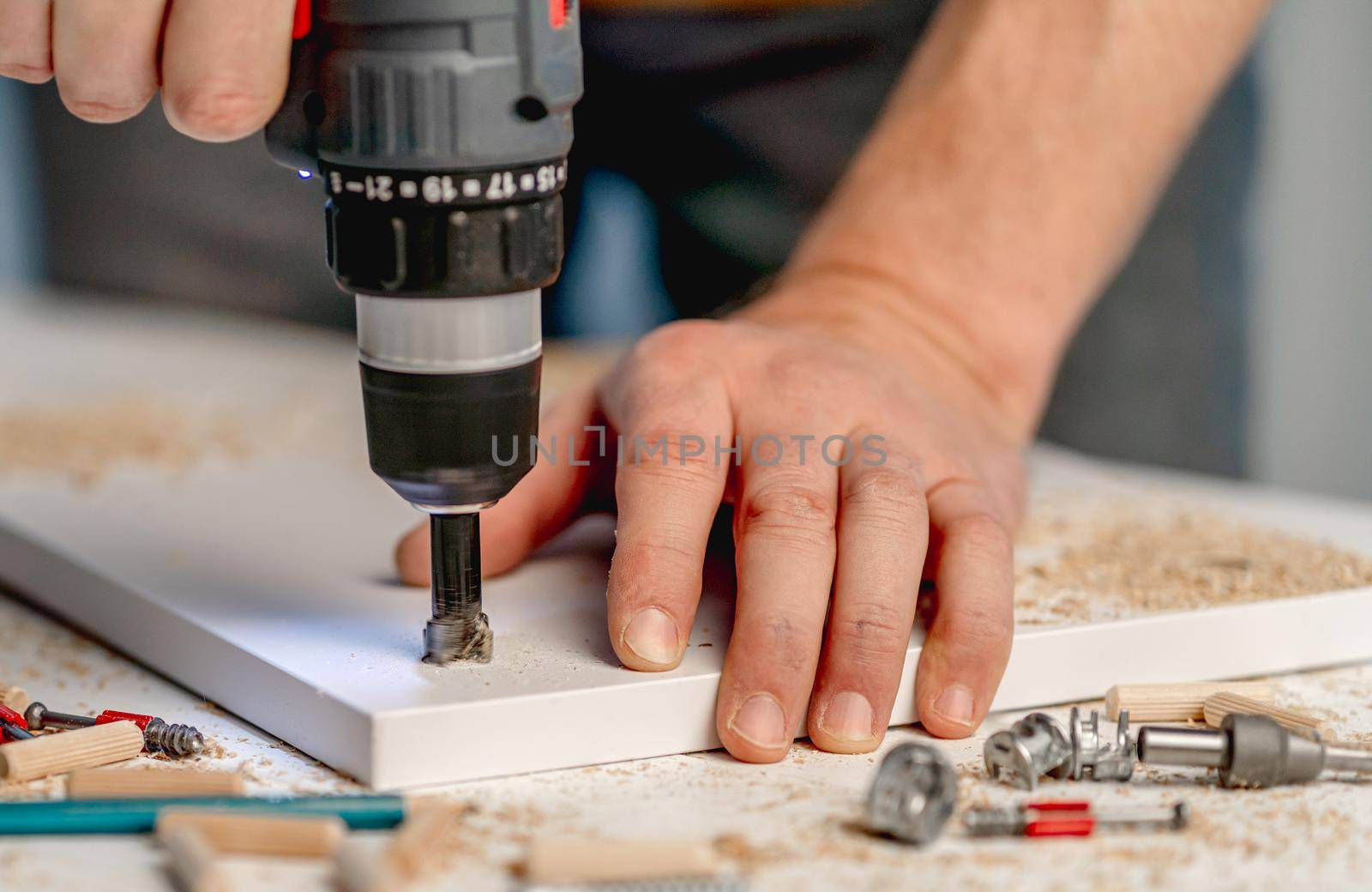 Man working using electric screwdriver during process of wooden furniture manufacturing in workshop