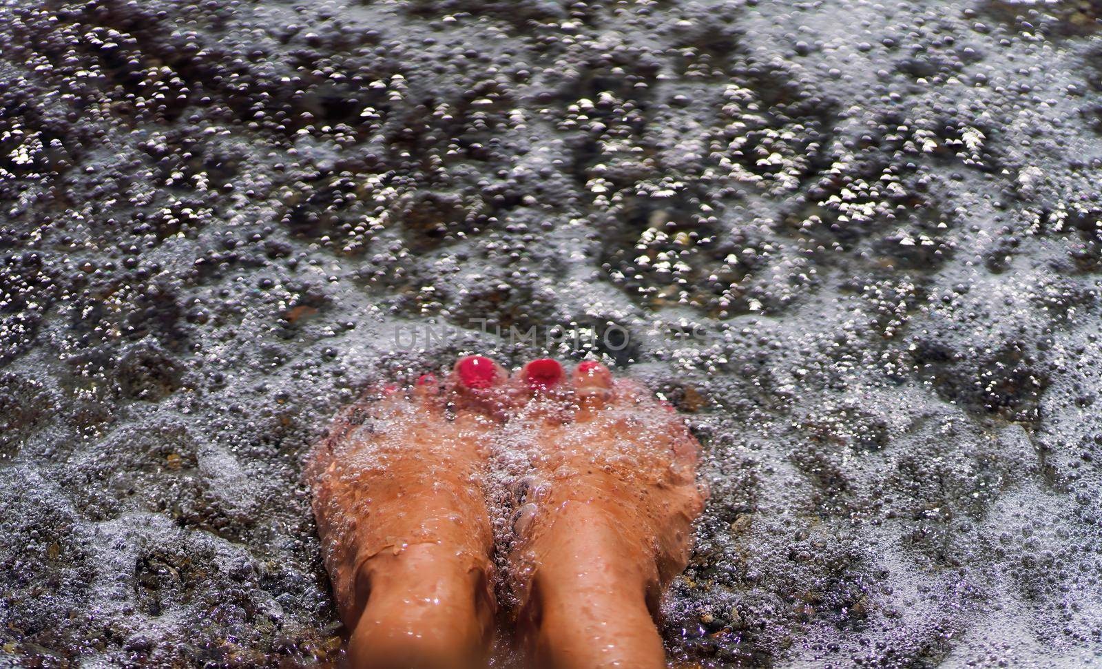 women's legs with a bright pedicure in the sand on the beach. summer holidays at sea