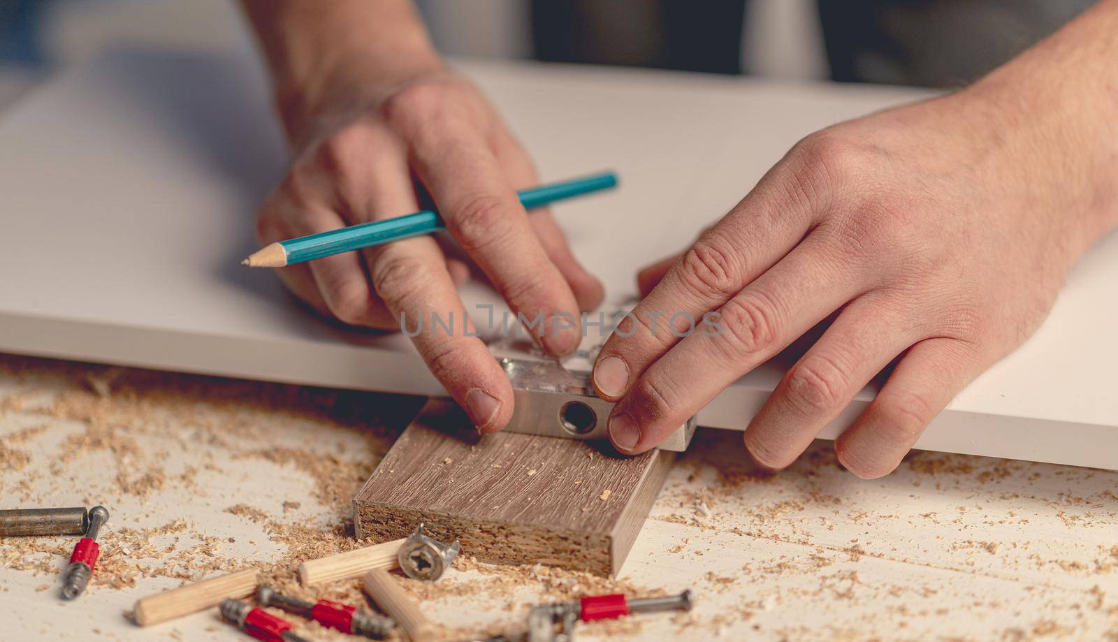 Man working using electric screwdriver during process of wooden furniture manufacturing in workshop
