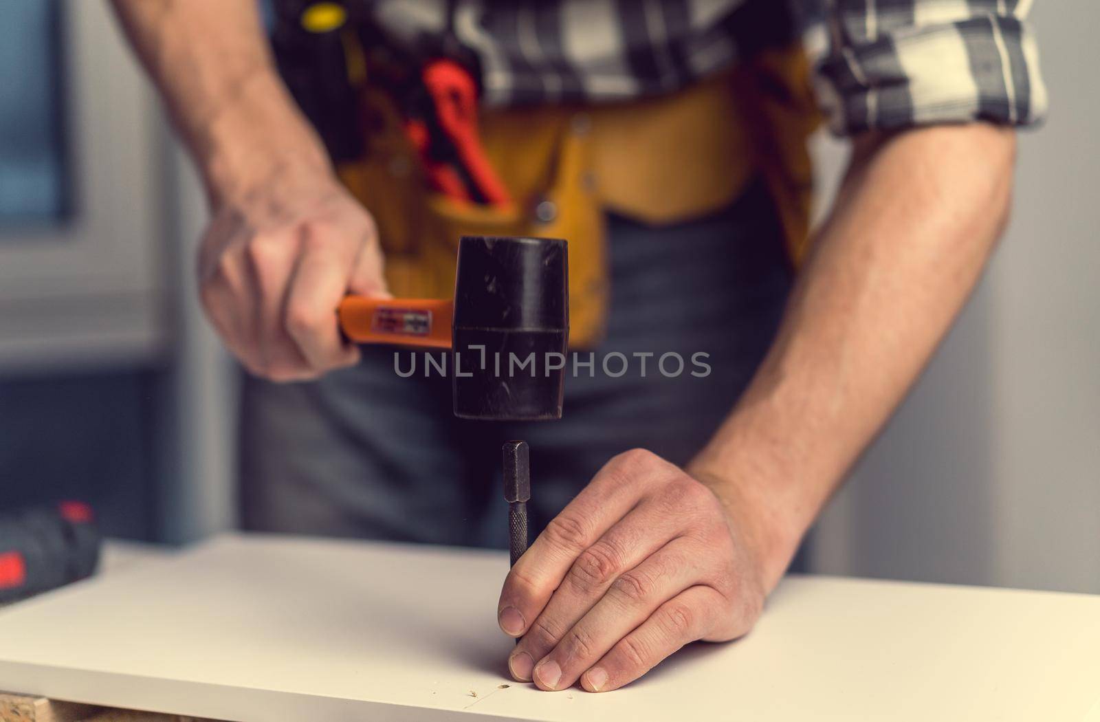 Man working with hammer and bit for hole during process of wooden furniture manufacturing in workshop