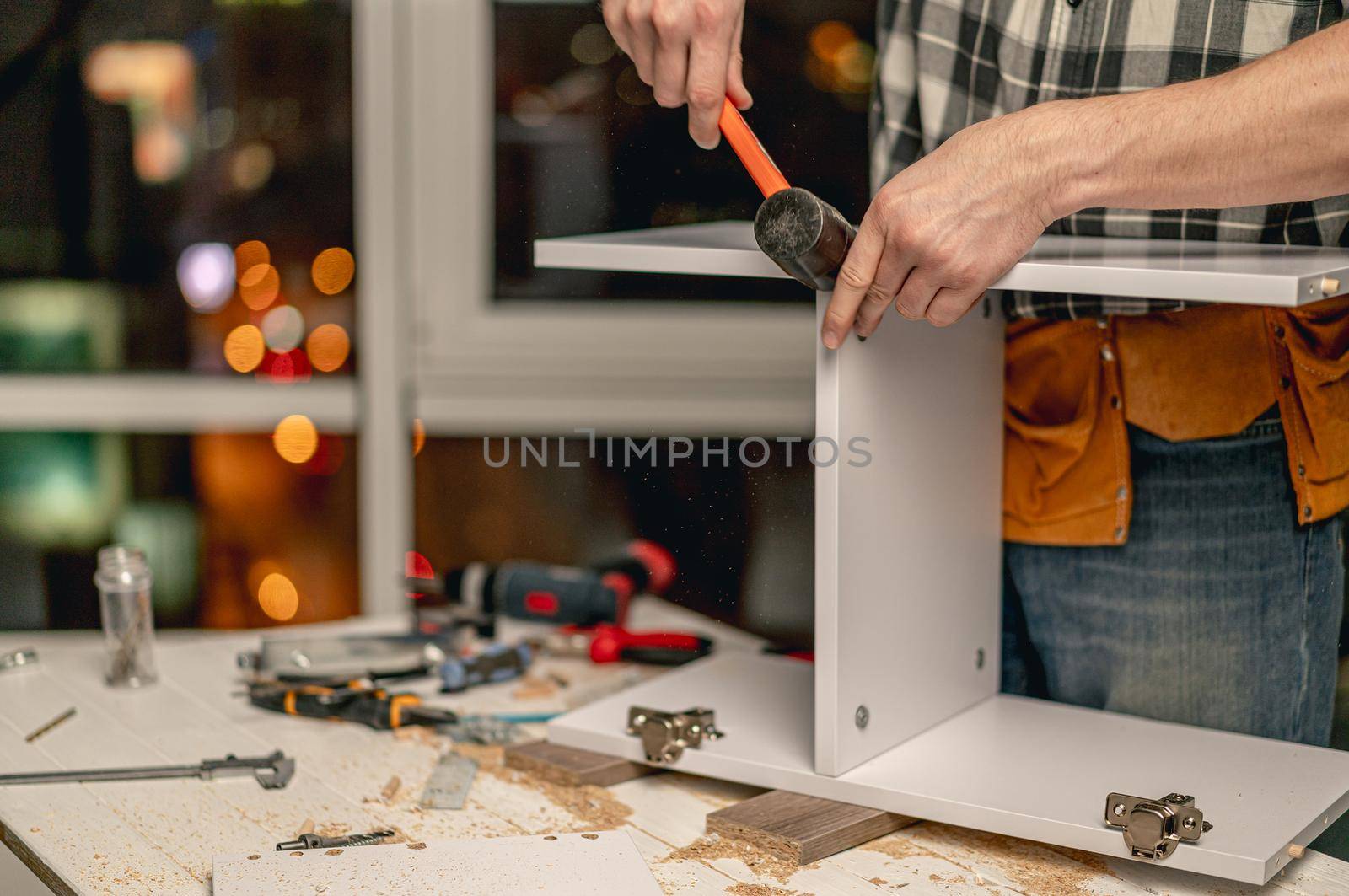 Man working using hammer for parts connection during process of wooden furniture manufacturing in workshop
