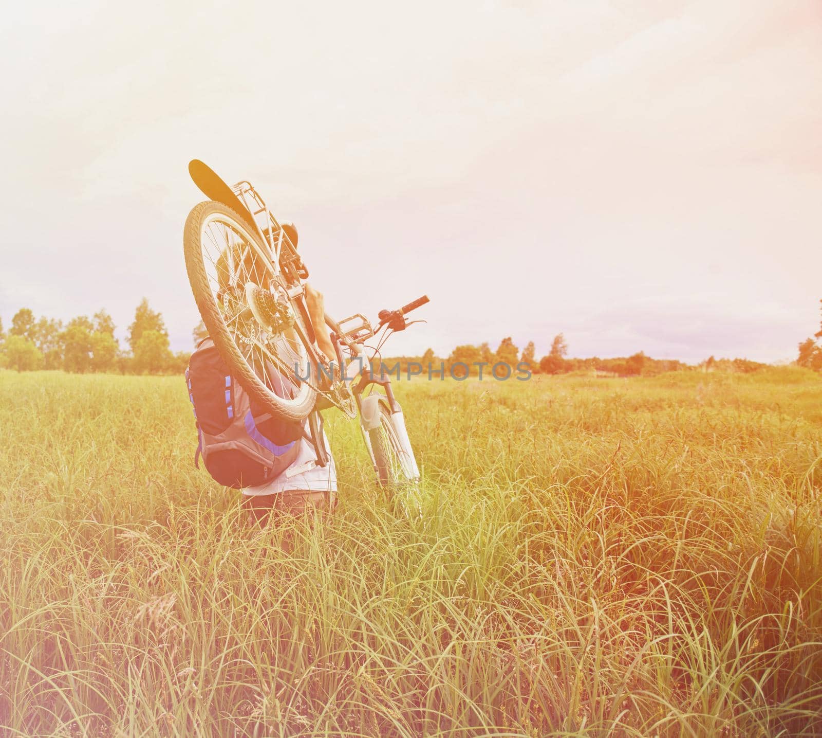 Cyclist carries bicycle in field by alexAleksei