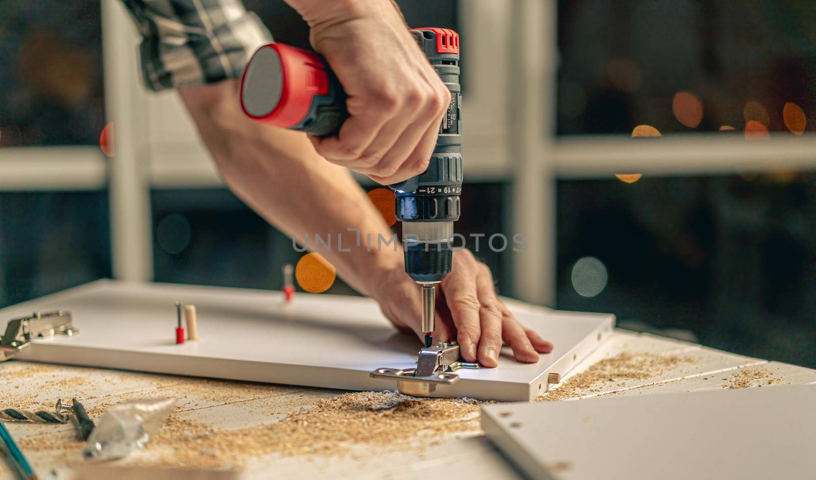Man working making holes in board with drill during process of furniture manufacturing