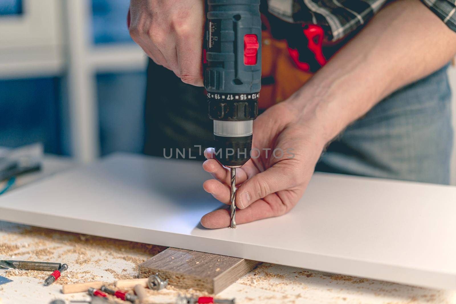 Man working making holes in board with drill during process of furniture manufacturing