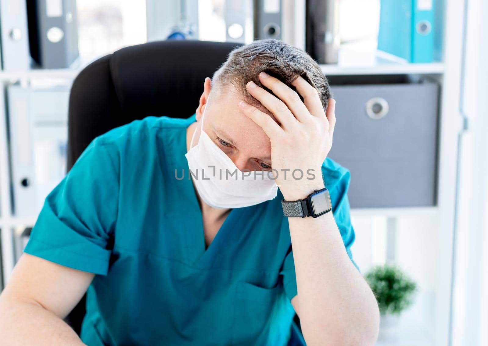 Exhausted doctor in medical mask sitting in office