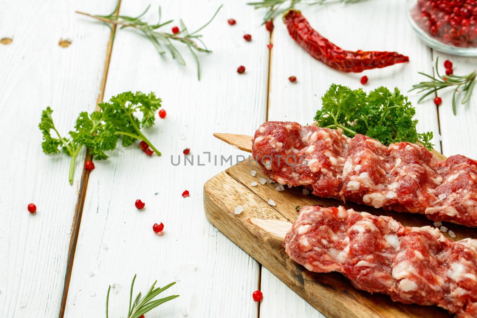 Raw lula kebab on skewers with spices on wooden board close up