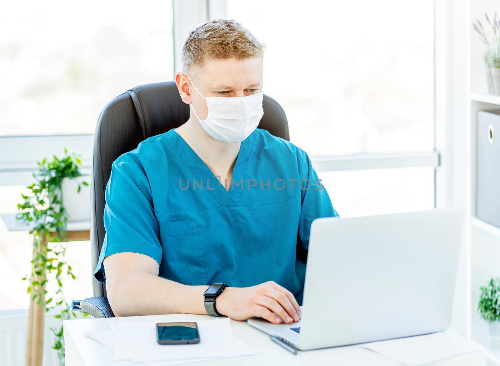 Doctor in face mask working on laptop in office