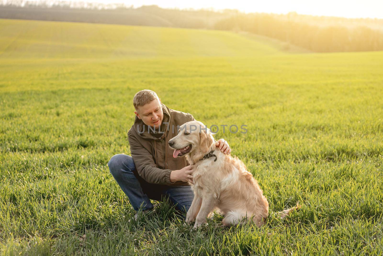 Handsome man cuddling cute dog outdoors on field