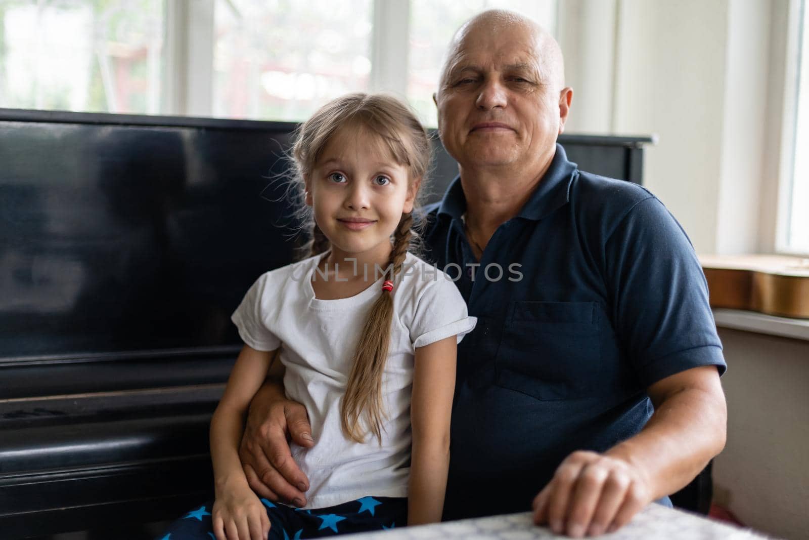 Senior grandfather with small granddaughter indoors sitting at table. by Andelov13