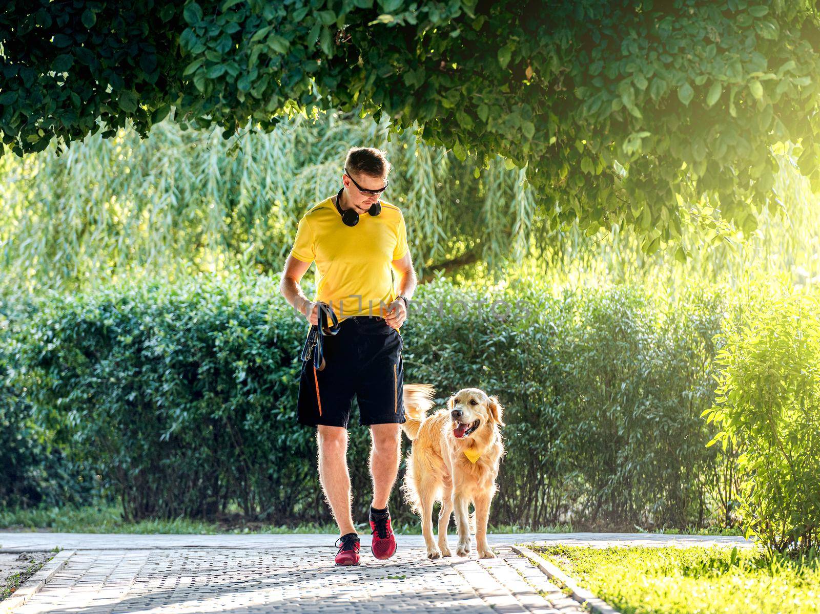 Young man jogging in park with golden retriever dog