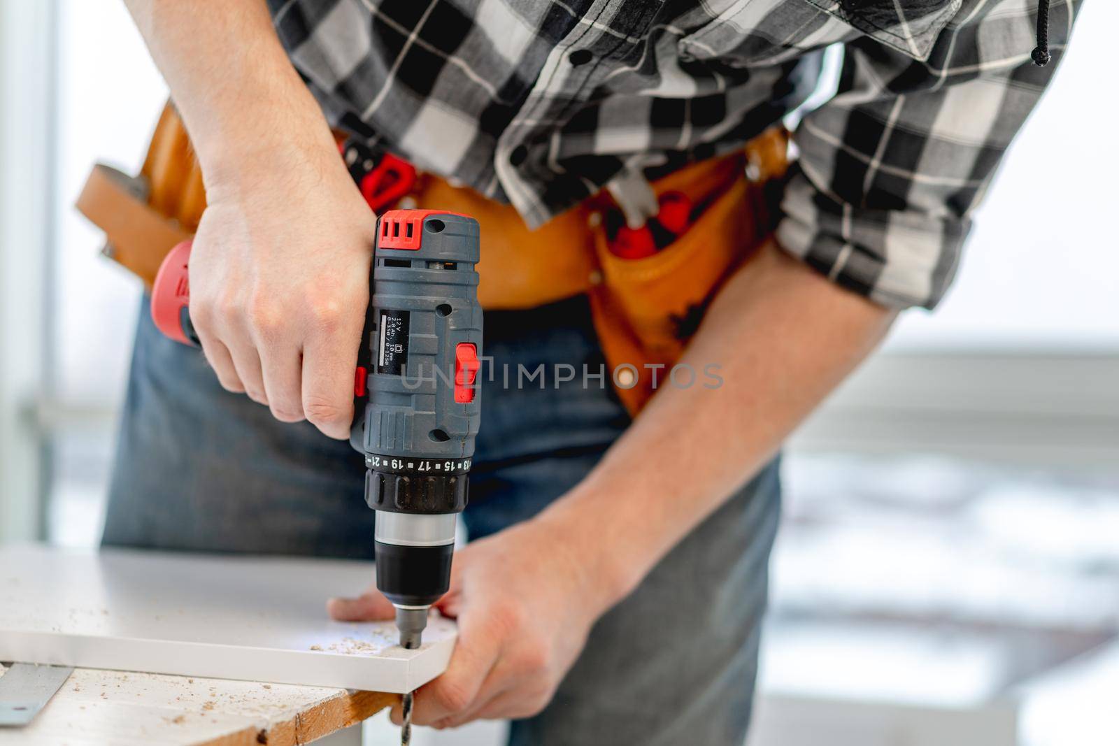 Man working using electric screwdriver during process of wooden furniture manufacturing in workshop