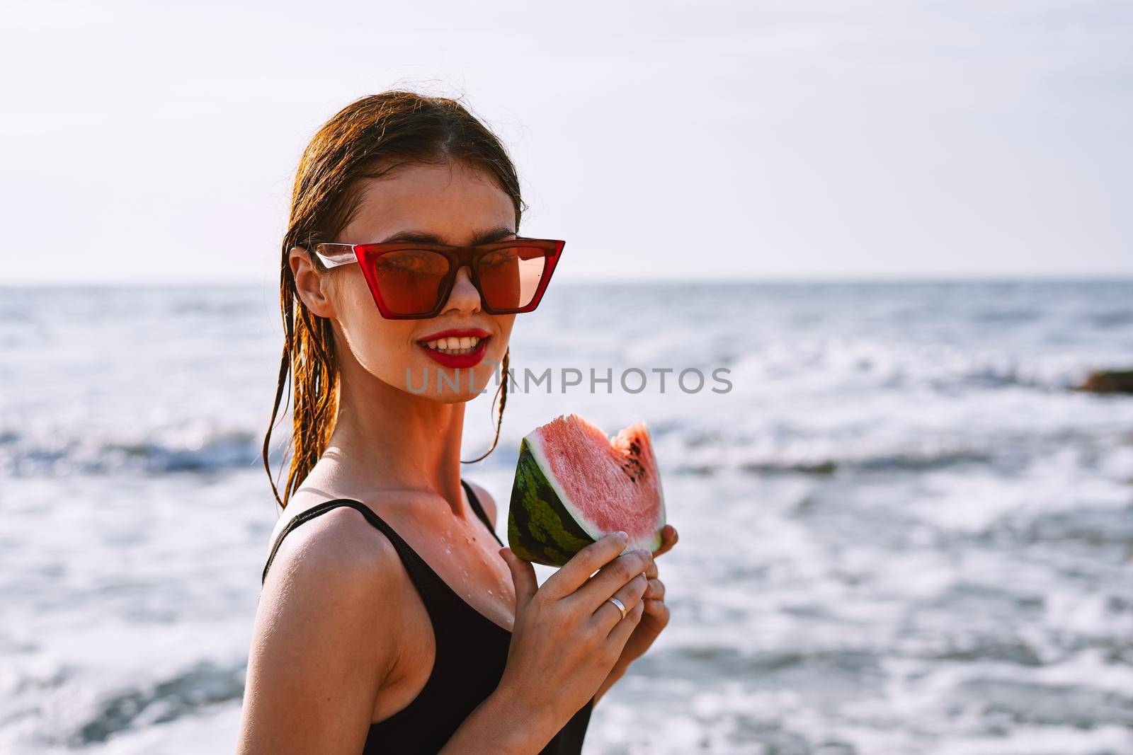 cheerful woman in sunglasses eating watermelon by the ocean. High quality photo