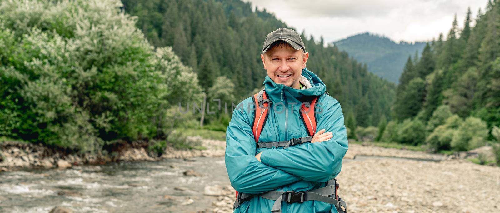 Smiling young man tourist with backpack standing on river mountain background