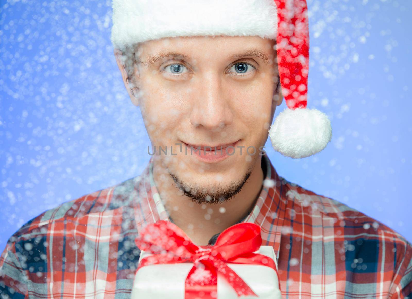 Happy young man in santa hat with a gift box in the snow