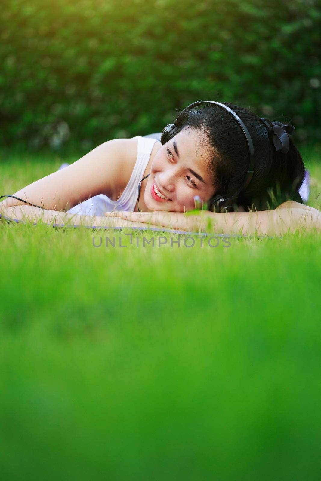 woman listening to music with headphones and laying on a grass field by geargodz