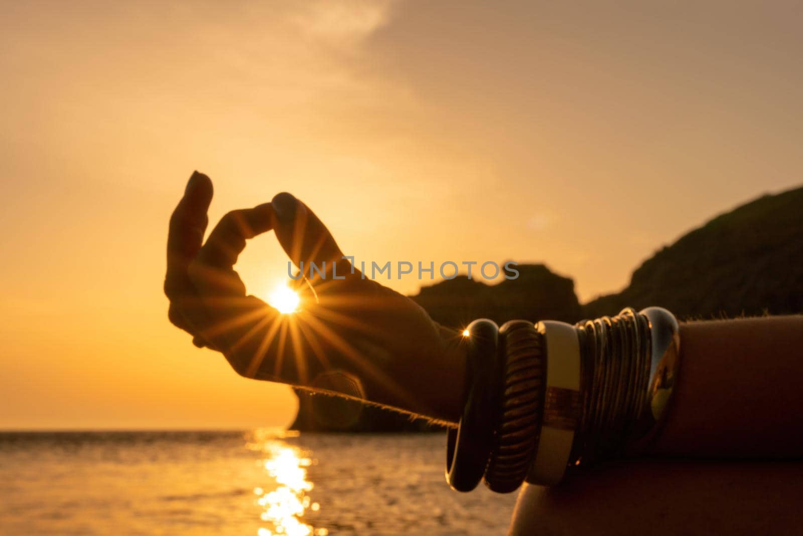 Young woman with long hair in white swimsuit and boho style braclets practicing outdoors on yoga mat by the sea on a sunset. Women's yoga fitness routine. Healthy lifestyle, harmony and meditation by panophotograph