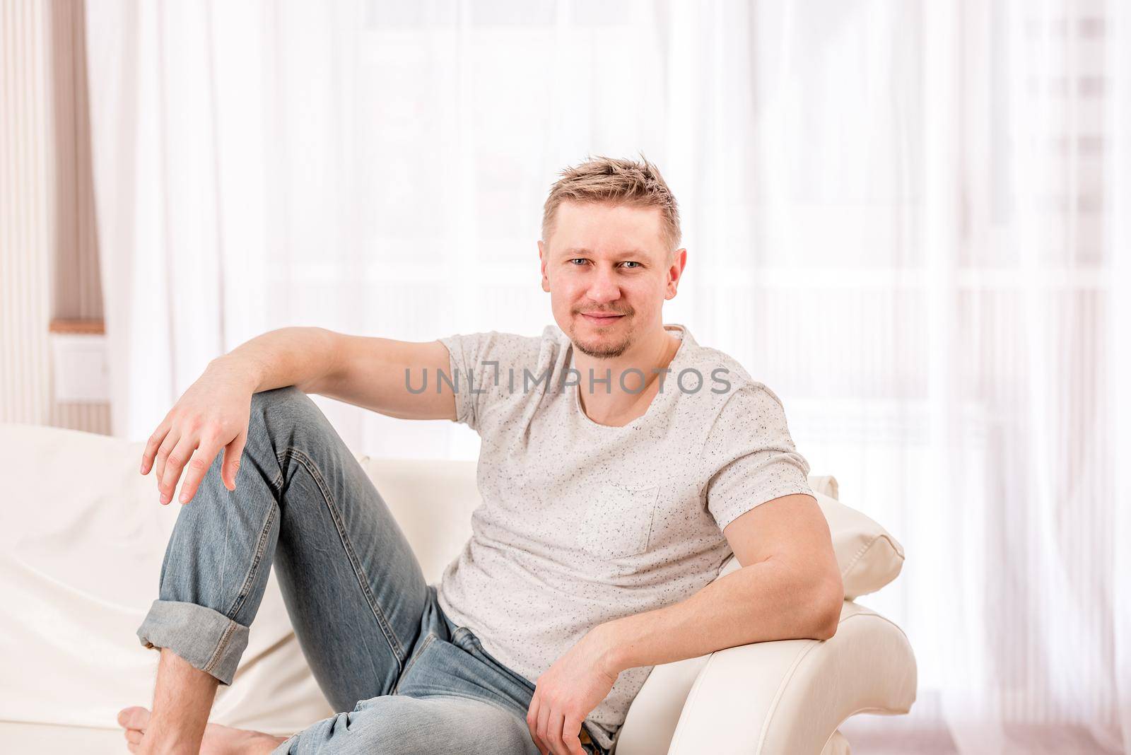 Modern man sitting on white sofa in bright bedroom