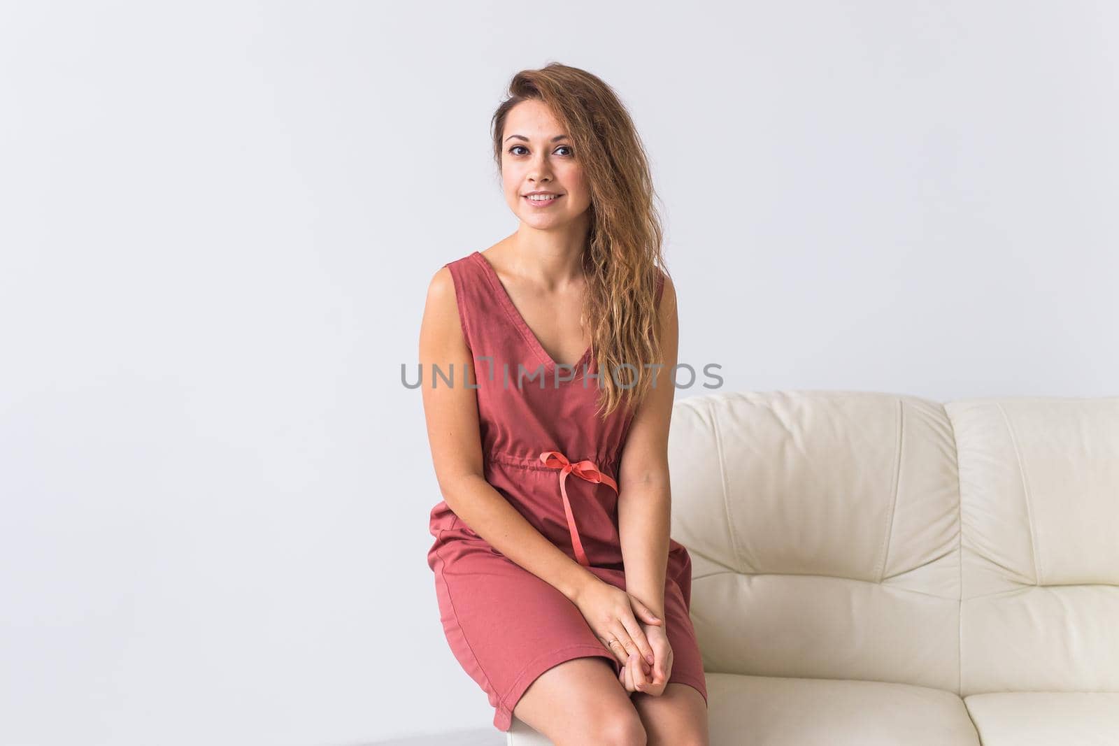 Young attractive woman dressed in beautiful home dress sitting on couch in her living room. Comfortable sleepwear, home relaxation and female fashion concept
